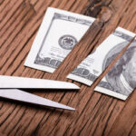 Cut Dollar Banknote and Scissor on Wooden Table
