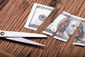 Cut Dollar Banknote and Scissor on Wooden Table