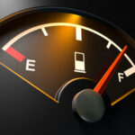 A closeup of a backlit illuminated gas gage with the needle indicating a near full tank on an isolated dark background
